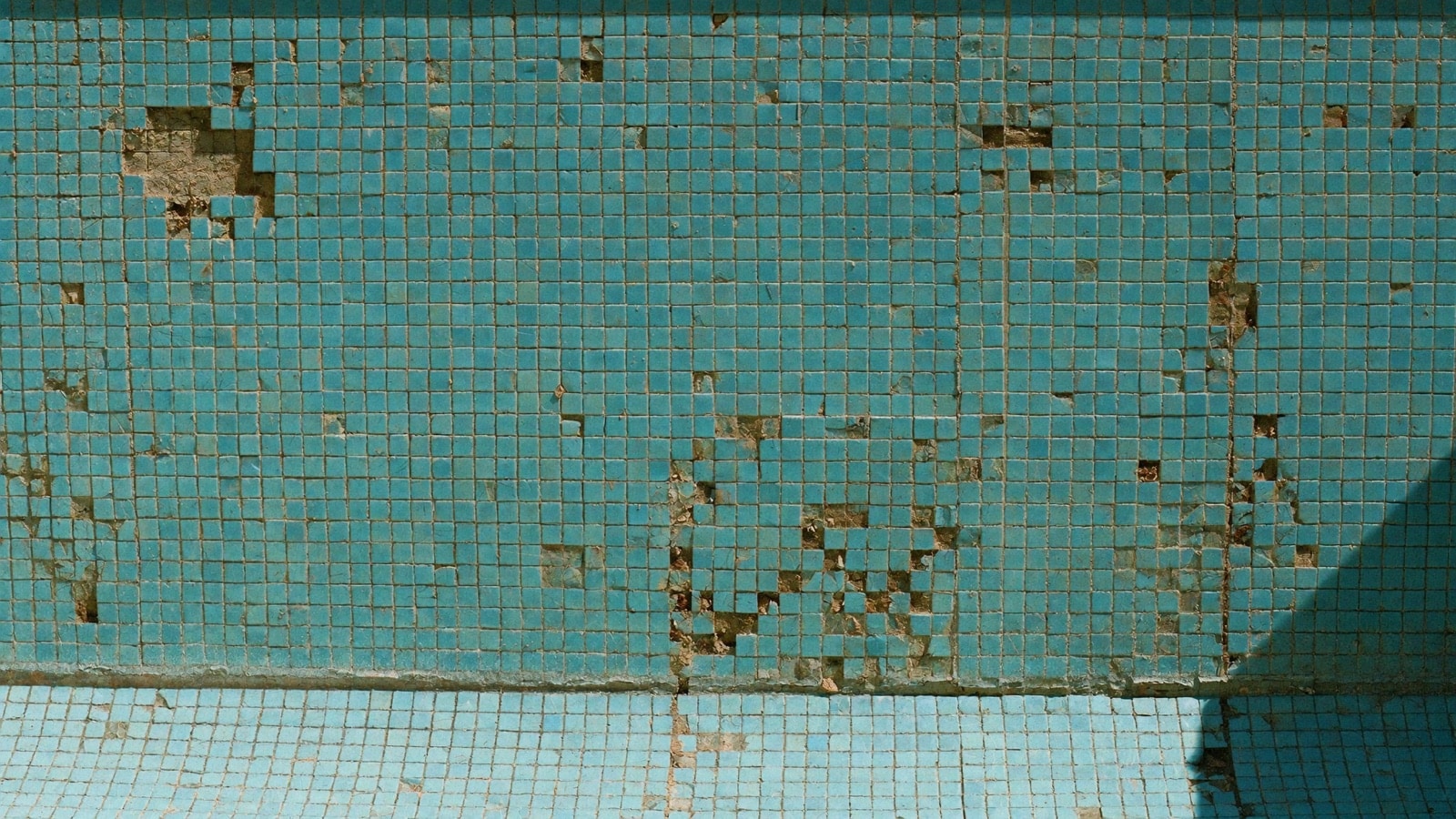 Mur de piscine vidée avec petits carreaux et joints abîmés