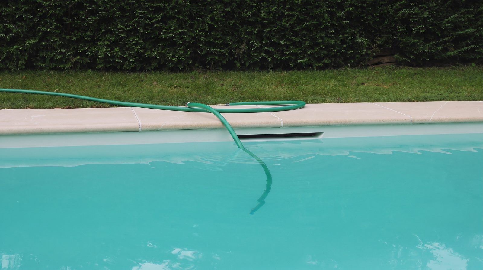 Tuyau d'arrosage posé sur la margelle, extrémité sous l'eau : remplissage d'une piscine